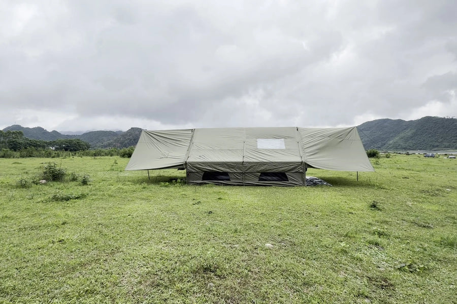 Army green Cabin tent with both extensions raised on a grassy campsite.
