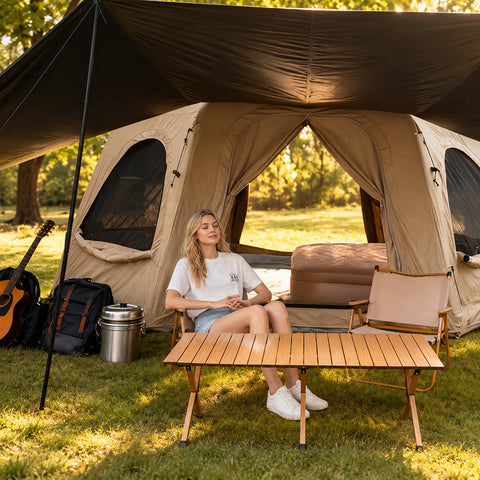 A camper seated at a table beneath the side awning of a khaki Dome tent.