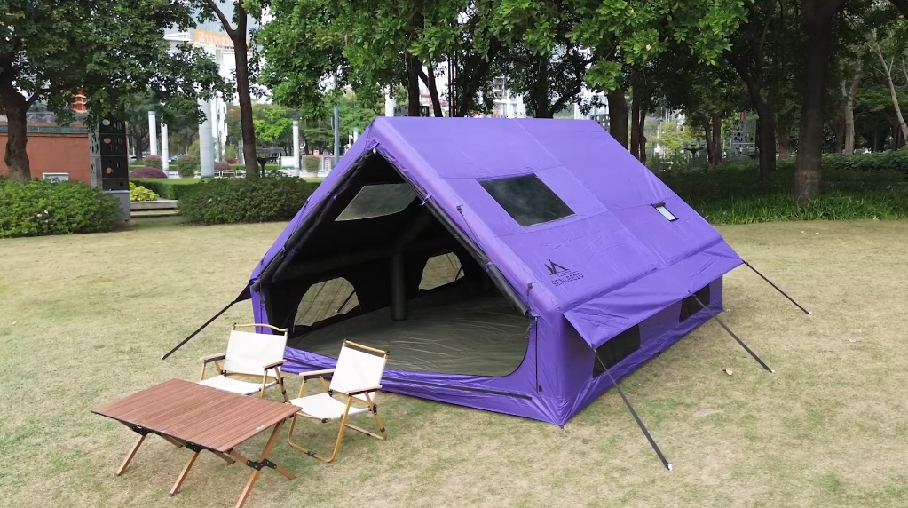Senleeto purple inflatable glamping tent set up on a grassy park with camping chairs and a table.