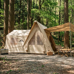 Exterior view of Senleeto Grand Air Cabin, a large 8-10 person inflatable glamping tent with stove jack and extended awning, set up in a lush forest camp site.