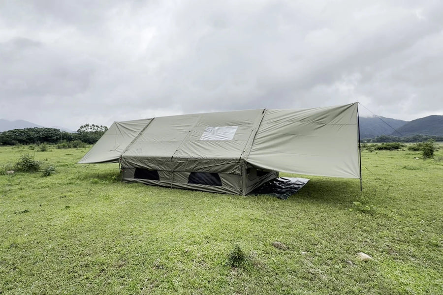 Army green Cabin tent with both extensions raised on a grassy campsite.