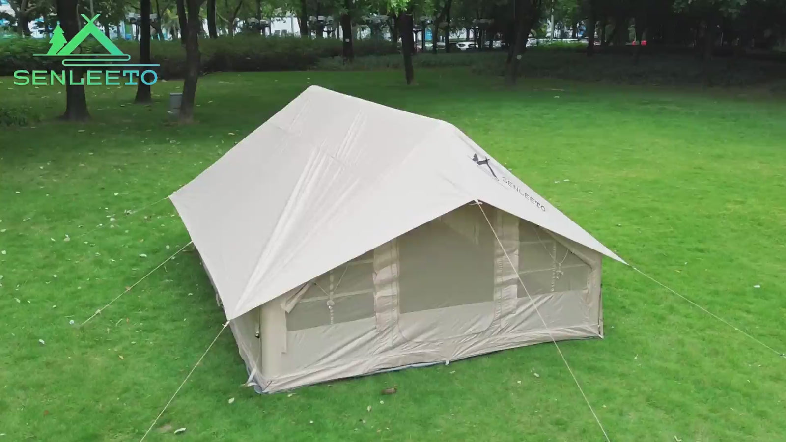 Senleeto large beige inflatable glamping tent with a 12sqm rain cover, setup on a lush green lawn in a park.